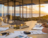 Bureau d'agence immobilière avec vue sur l'île de Moorea, table avec documents immobiliers, maquette de villa et mains d'agent immobilier conseillant un client
